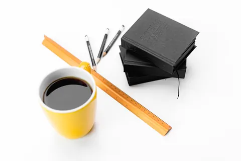 A stack of the black Poems notebooks beside a yellow mug of coffee, pencils and a ruler
