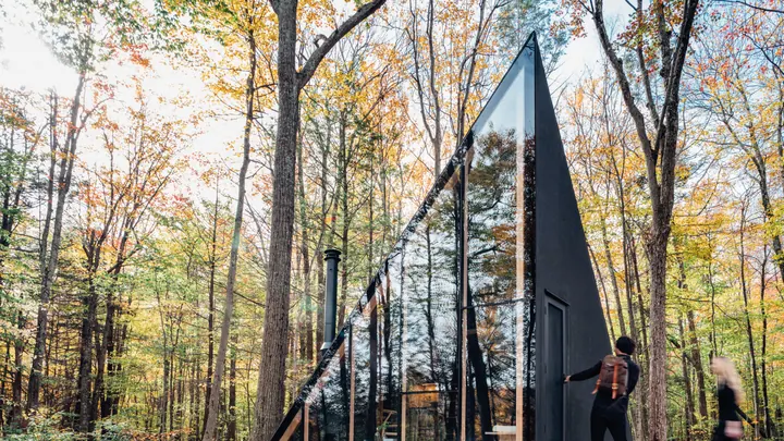 The black A45 among autumn trees, its tall triangular glass end reflecting the forest, two people walking by