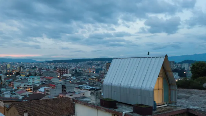 The silver A-frame on a flat roof above Quito at dusk, the city spread out below