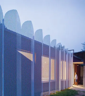 The Urban Cabin behind a blue perforated metal screen with arched tops, lit at dusk