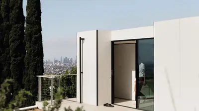 A white box with a black glass door on a terrace, a city skyline in the haze behind