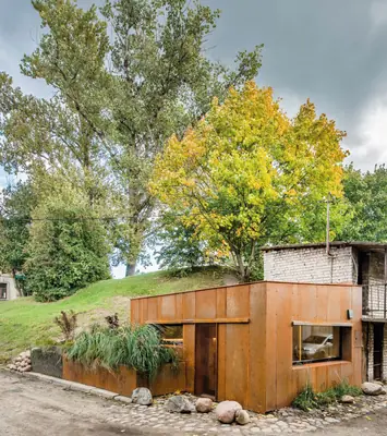 The Corten steel garage home under tall trees, planted up against a grassy bank