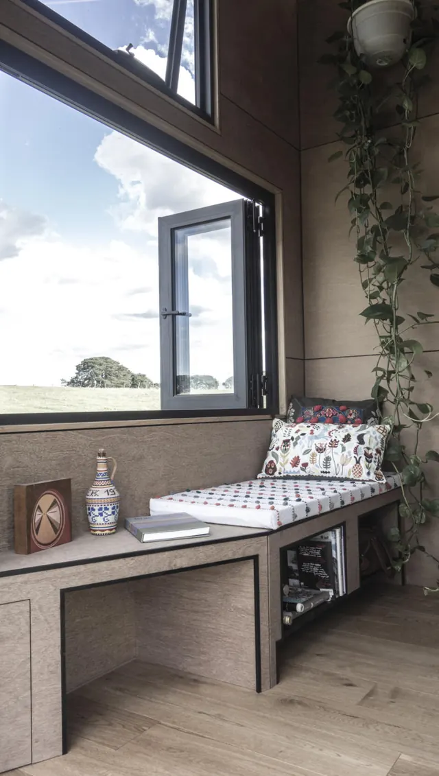 A cushioned ledge and a counter under a big window onto the fields, plants hanging beside it