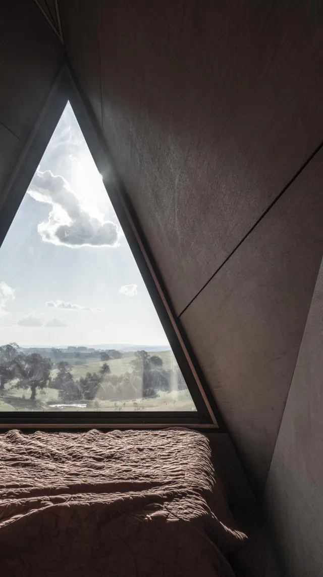 Lying in bed under the A-frame, the countryside framed by a triangular window