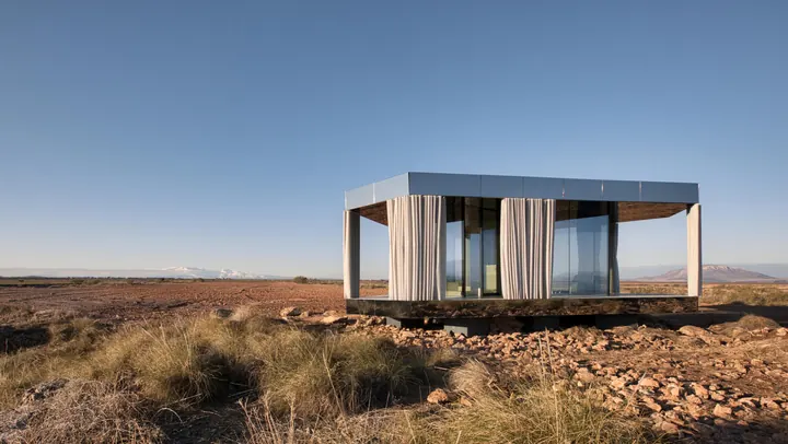 The Glass House on a rocky desert plateau, a flat timber roof on walls of glass under a clear sky
