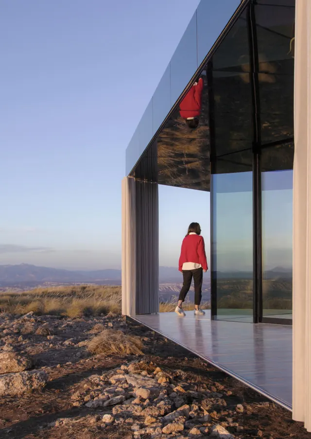 A woman in red on the porch, the desert reflected in the glass walls beside her