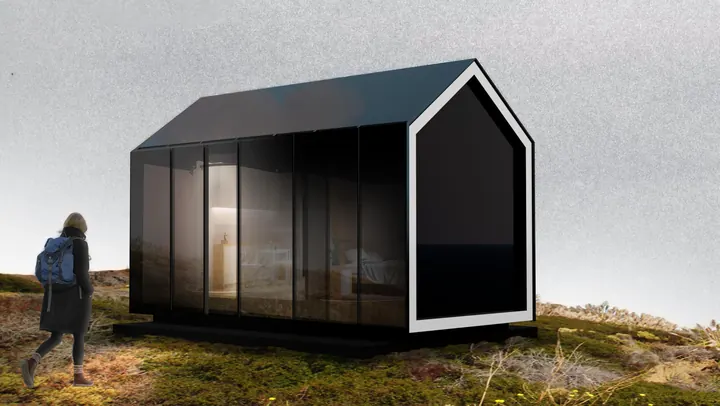 The black gabled Revolve Microhome on a grassy hilltop under a grey sky, a walker passing