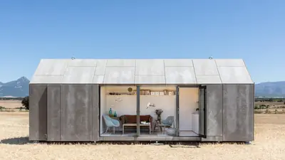A grey gabled cabin with its glass doors open onto a dry plain