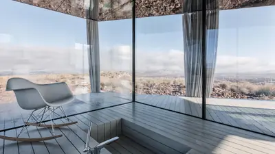 Inside the Glass House: a rocking chair behind floor-to-ceiling glass, the desert beyond