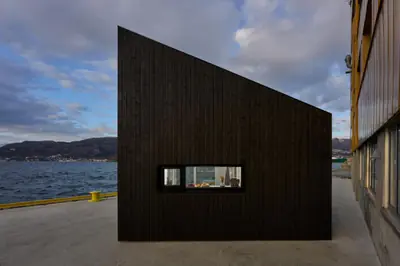 The black cabin with a narrow window strip, standing by the harbour water