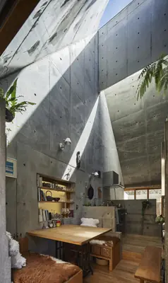 Inside Love2 House: concrete walls rise to a curved roof open to the sky above a dining table