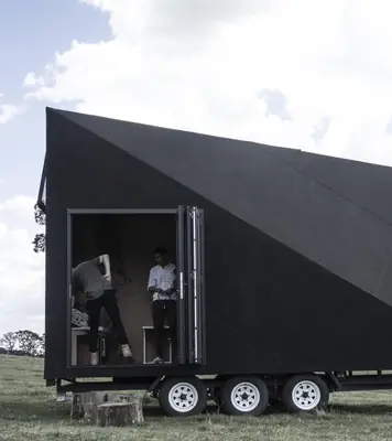 The black A-frame cabin on its three-axle trailer, its glass door open