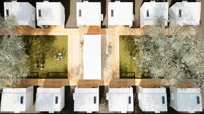 A village of small white pods from above, around a shared garden and a long table