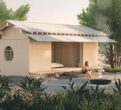 A low timber house with a wide eave and a round window, set in a garden of rocks and plants