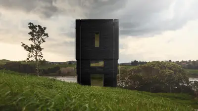 A tall black tower house on a grassy hill under a stormy sky