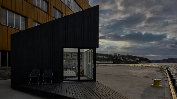 The black XS Micro House on the docks of Bergen at dusk, its terrace facing the water