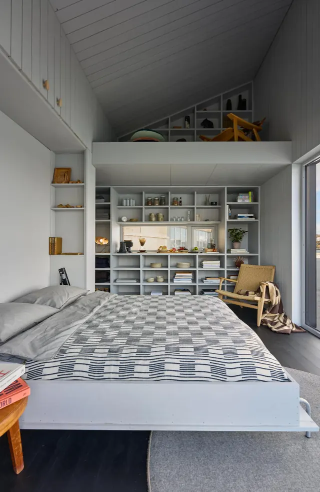 A bed with a checked blanket in front of a wall of open shelves