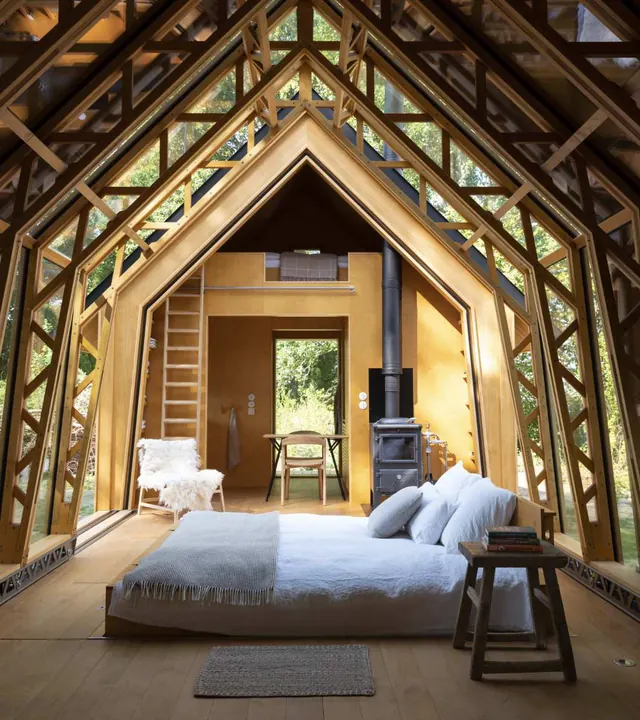 Inside: a wide bed under the pale timber frame of the gable, a stove and an open door at the far end