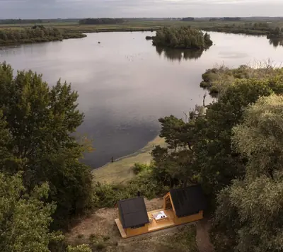 Cabin ANNA from above by a lake in the heath, its two roof halves pulled apart