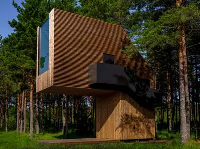 The timber treehouse among pine trunks, its big window and a small balcony high above the ground
