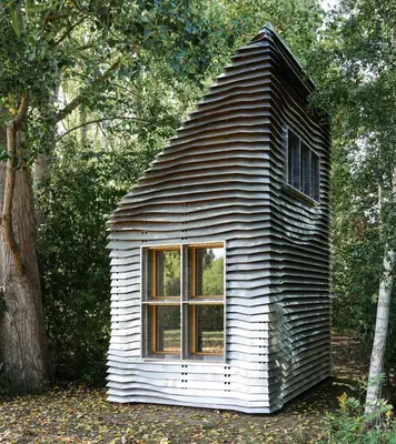A tall narrow house with a steep roof, clad in rows of bent aluminium sheets, among trees