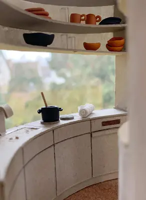 A model interior: a curved kitchen counter under a window, with small pots and bowls on the shelves