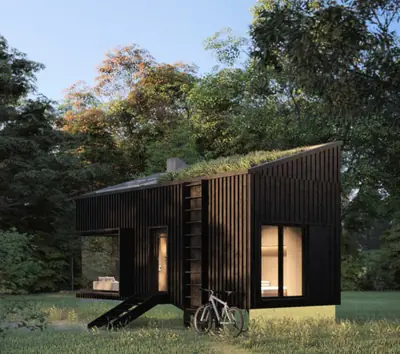 A black cabin with a planted roof and a ladder, lit from inside, in a green wood