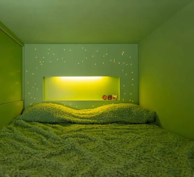 The low bedroom: a green bed filling a green room under a lit shelf with small star lights