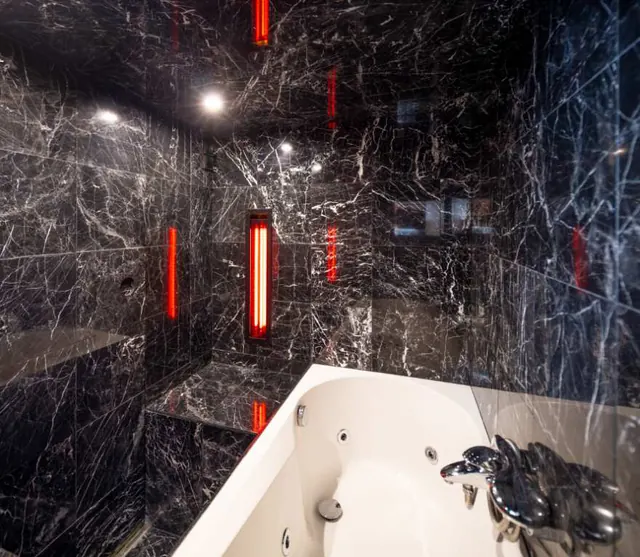 The spa: a white bathtub in a room of black marble, red infrared lamps on the walls