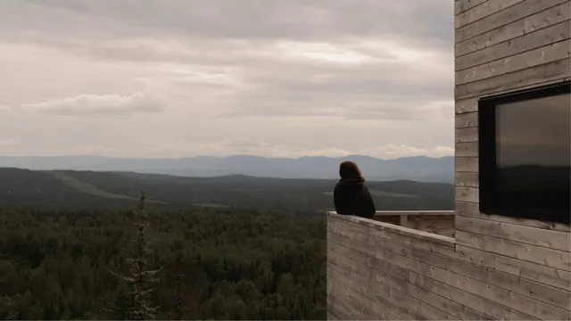 Someone on a timber terrace looking out over forested hills to a far range of mountains