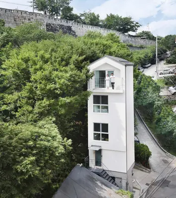 A narrow white house five floors tall on a steep street, trees all around it