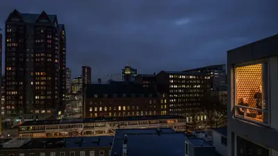 Rotterdam at dusk from a roof, and at the right the lit window of the Cabanon in an attic