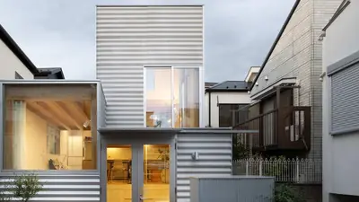 The street front: walls of corrugated metal and a big window onto a lit timber room, neighbours close on each side