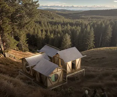 Four small houses in a ring on a forested hillside, their roofs pitched different ways