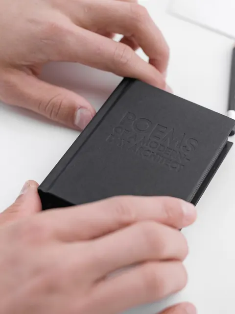 Two hands holding the closed notebook, which fits between them
