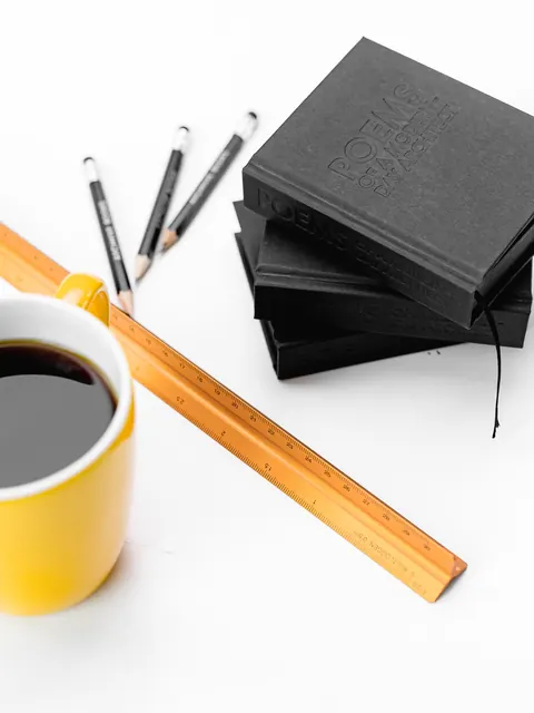 A stack of the notebooks beside a yellow mug of coffee and three pencils