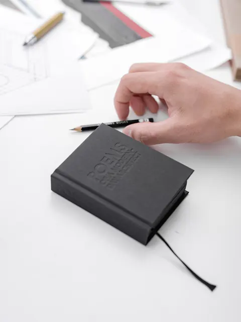 A hand laying the pencil on the closed notebook, its ribbon trailing