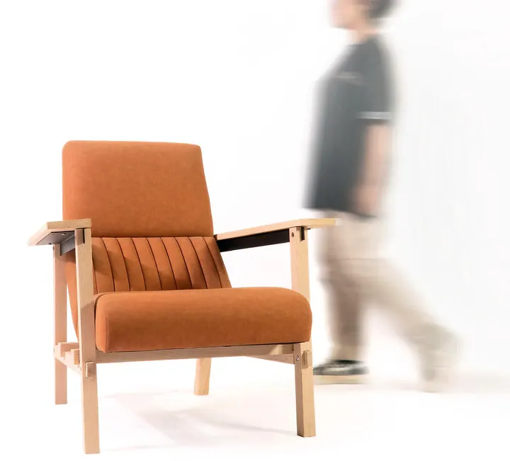 The 100.BUT armchair in pale wood with orange upholstery, a person walking past