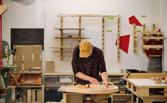 A maker at the bench in the workshop, Elsie chair parts on the wall