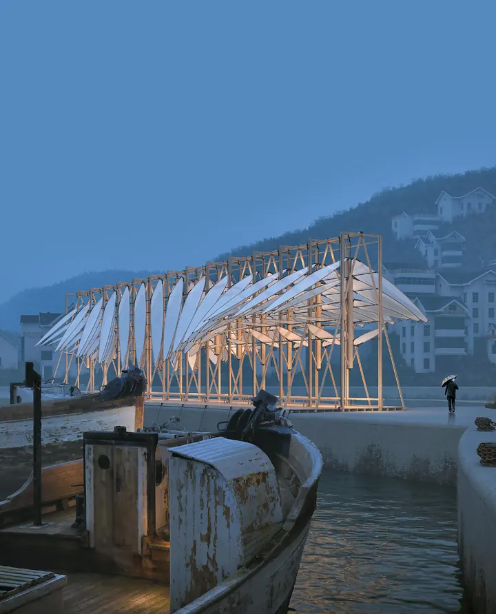 Le pavillon au crépuscule sur la digue du port, ses ailes blanches éclairées, un vieux bateau de pêche au premier plan