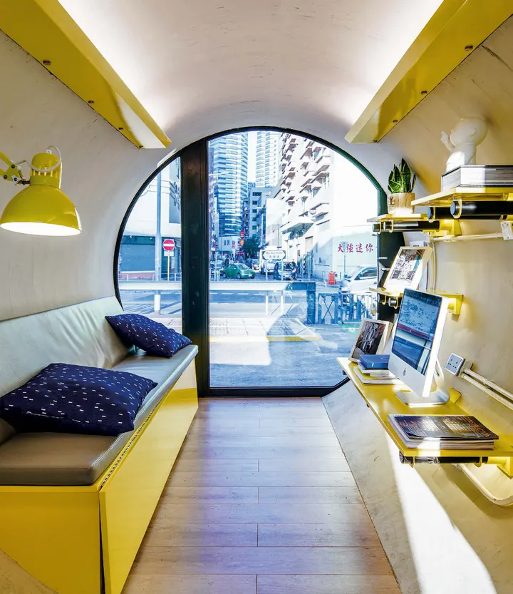 Inside an OPod: a curved white shell, a yellow bench and desk and a round window onto the street