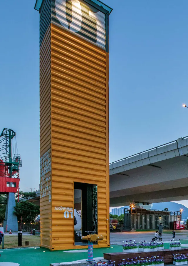 An orange container tower at dusk beside a motorway flyover