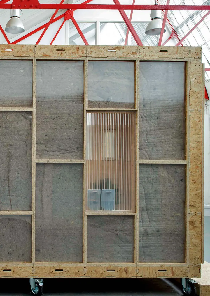 The Shed, a timber box with translucent panels, standing under the red steel roof of a warehouse