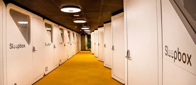Una hilera de habitaciones Sleepbox a lo largo de un pasillo con alfombra amarilla