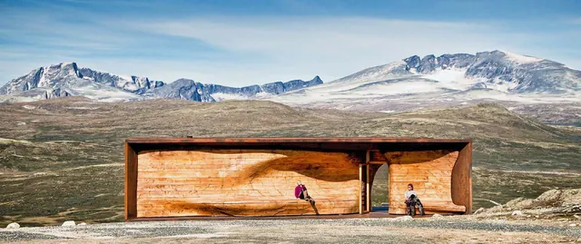 El pabellón en la meseta, con montañas nevadas detrás y dos personas en su banco