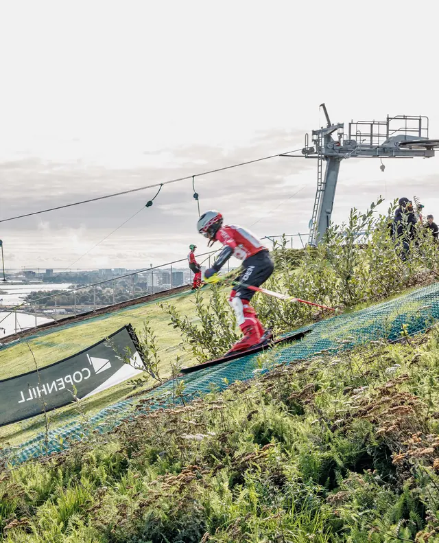A skier on the green slope, the lift and the harbour behind
