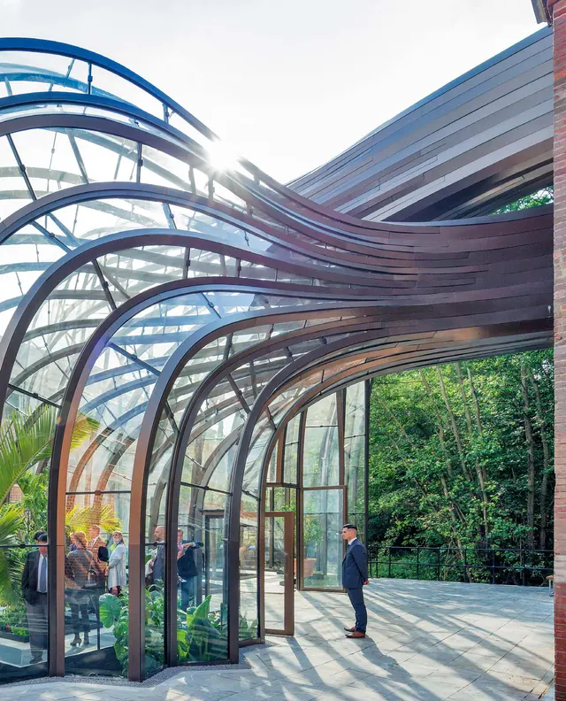 The glasshouse ribs sweeping into the brick stillhouse, visitors inside